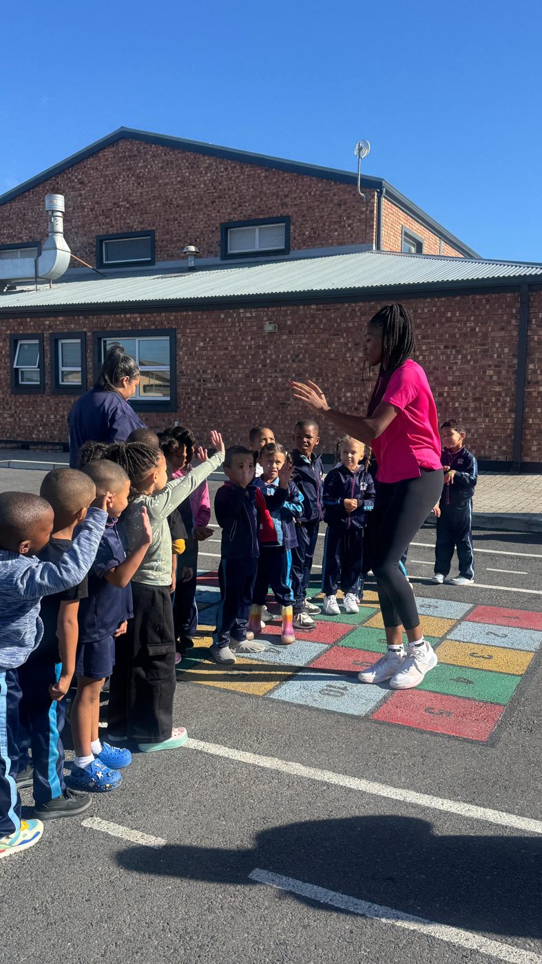A DSL coach leading a netball warm-up with a line of Bundles of Joy learners with their hands raised