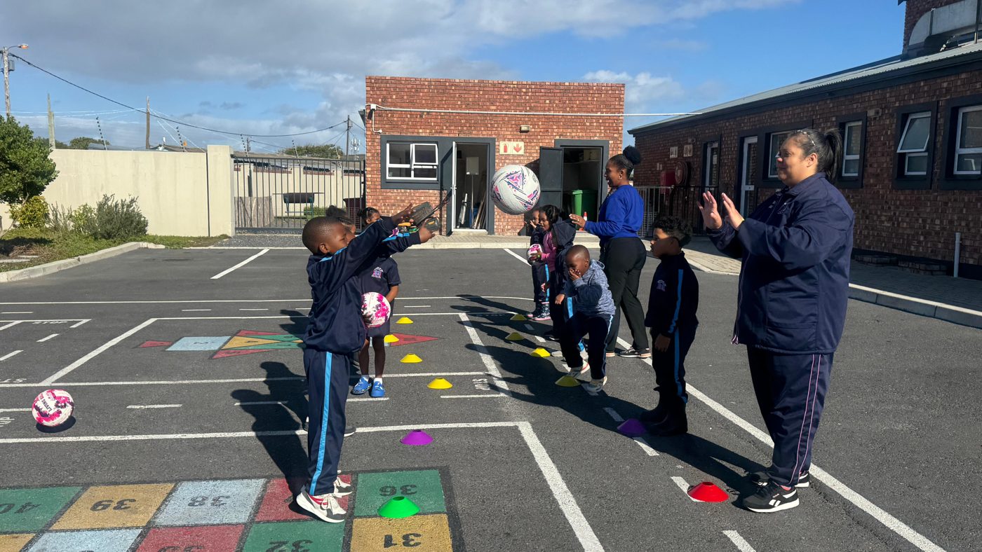 Learners tossing netballs at the cone stations while the centre's teacher looks on