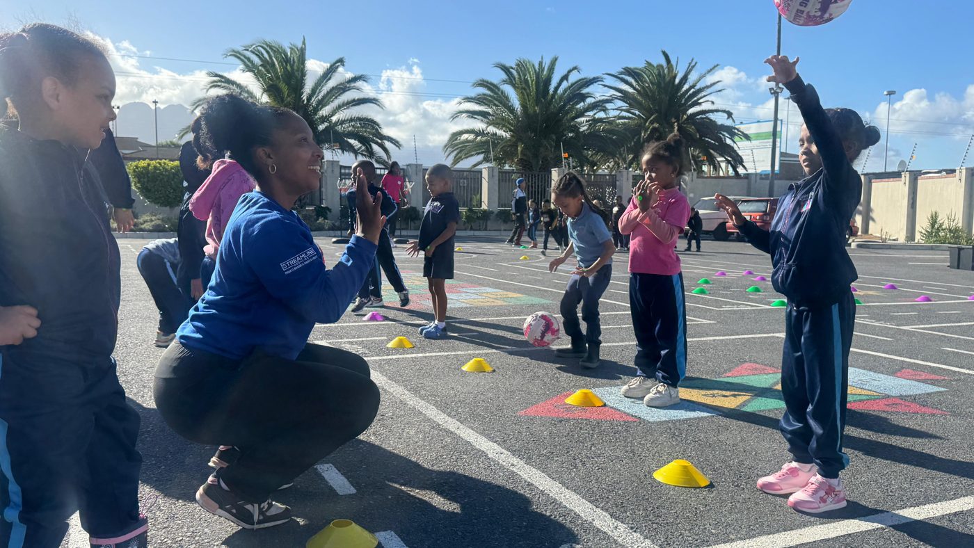 A DSL coach crouching to practise catching with learners at Bundles of Joy