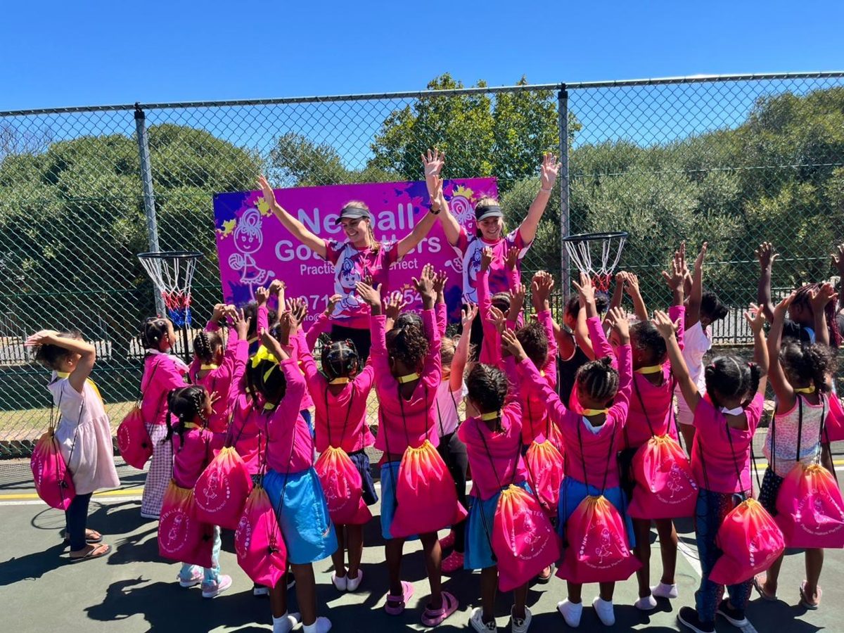 Children in pink Goal Getters bibs with their hands raised at a netball outreach session